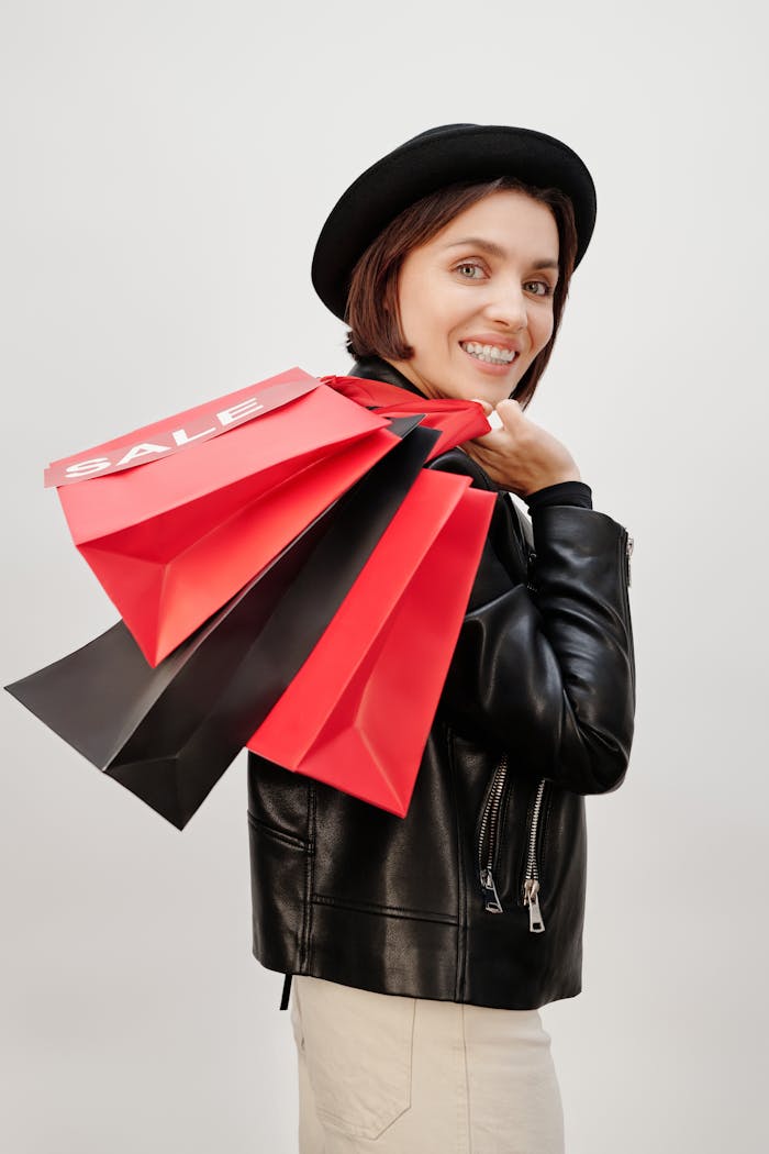 Smiling woman in black hat holding red and black sale shopping bags, representing modern consumerism.